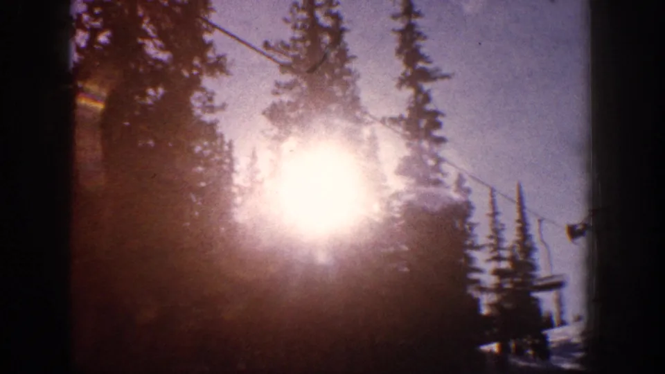 1961 Aspen frame with intense sun glare behind silhouetted evergreens and a ski lift cable crossing the winter sky.