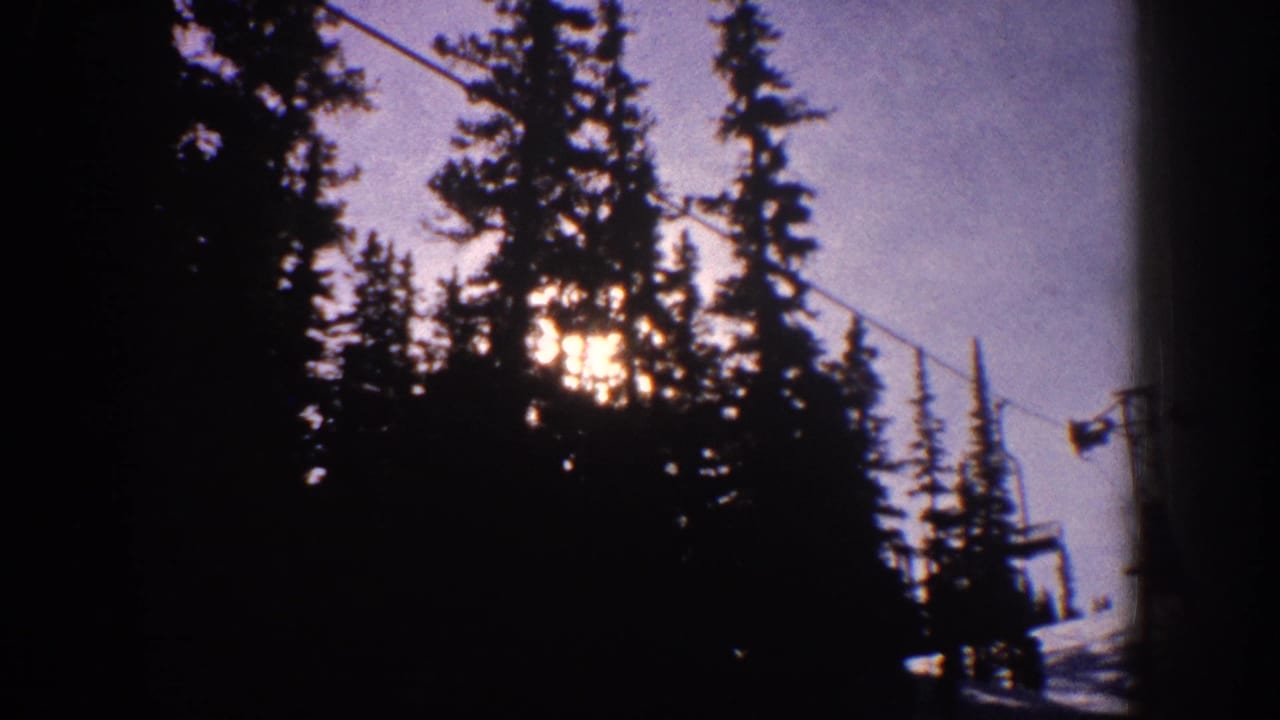 1961 Aspen-area ski scene with low sun behind tall pines, a ski lift cable crossing the frame, and snow visible near the lower edge.