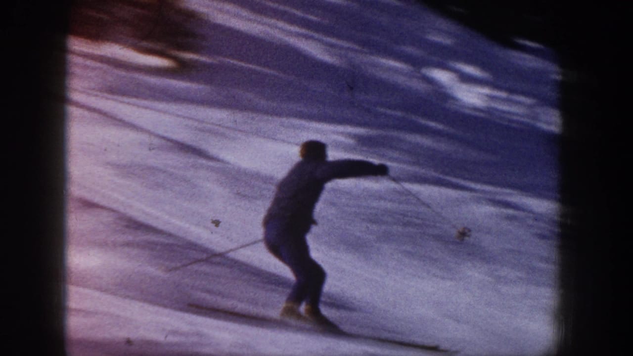 1961 Aspen home-movie frame showing a skier in dark winter clothing moving across a snowy slope with trees beyond.