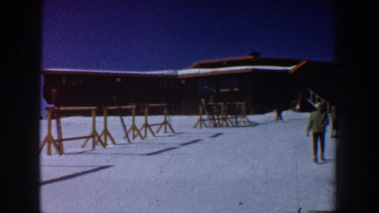1961 Aspen ski-resort footage showing a lodge, empty ski racks, bright snow, and a skier walking near the frame edge.