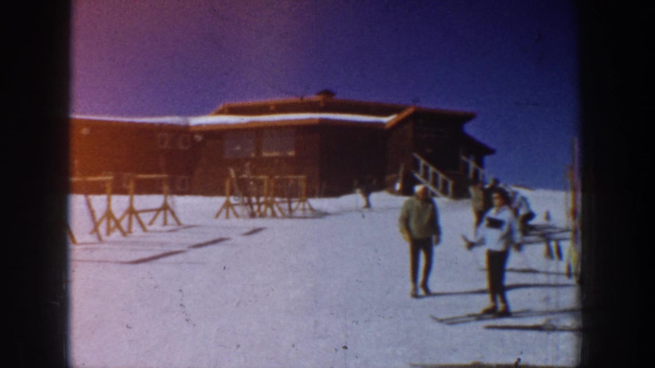At an Aspen ski resort in 1961, several skiers move across the snow near a wooden lodge and mostly empty racks.
