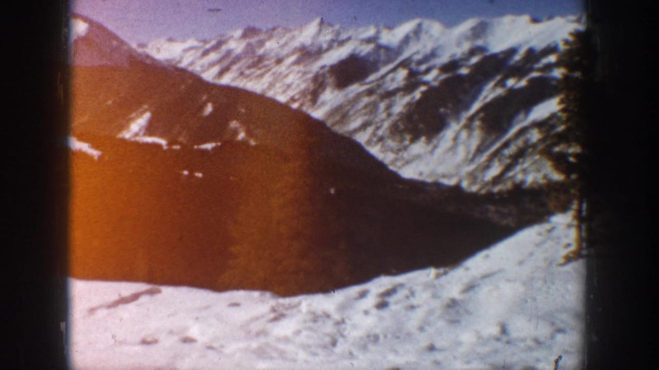 Aspen, Colorado winter landscape in 1961 home-movie footage, with snow-covered peaks, a dark hillside, and visible film gate edges.