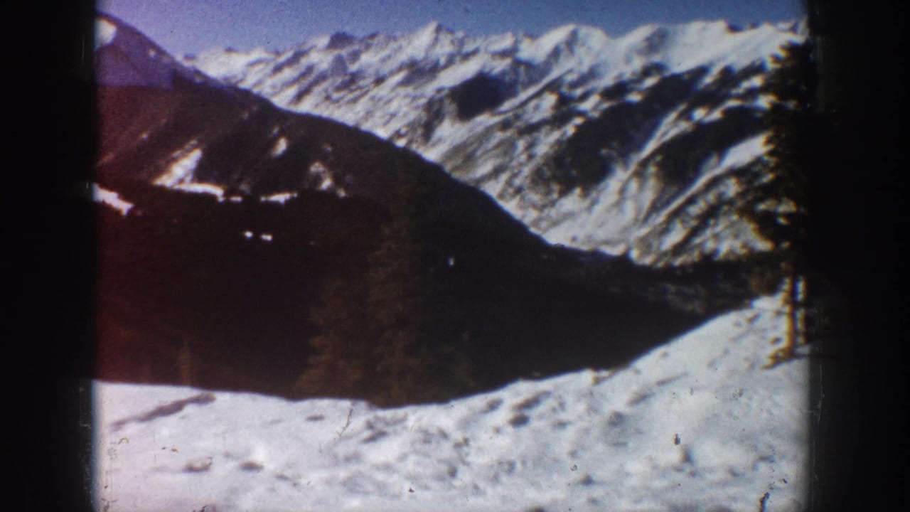 1961 Aspen winter view with snow-covered mountain ridges, a dark foreground slope, scattered evergreens, and soft 8mm color.