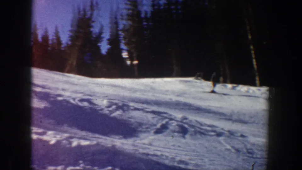 1961 Aspen ski scene with one skier descending a small snow-covered slope near dark evergreen trees.