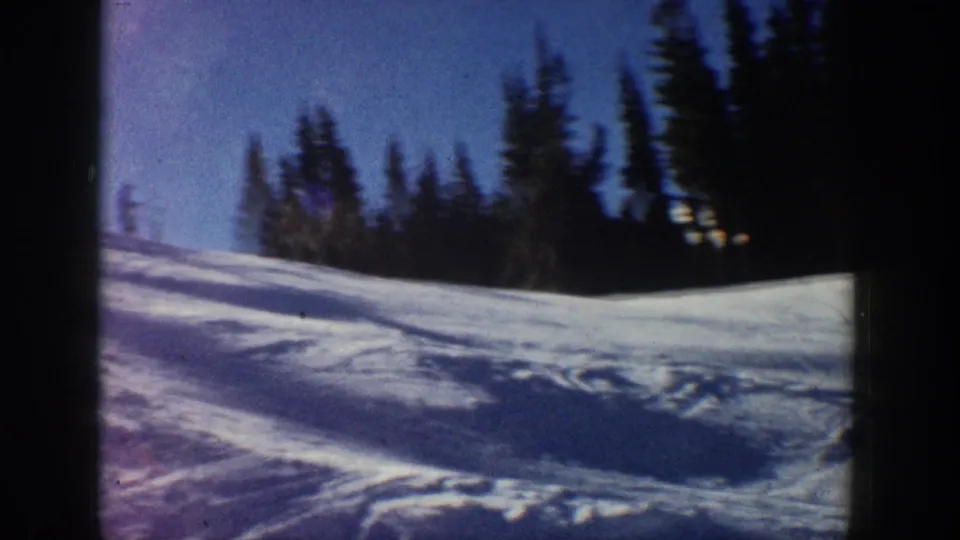 Soft 8mm frame from Aspen in 1961 showing a snowy ski slope, evergreens, and a small distant skier at the edge.