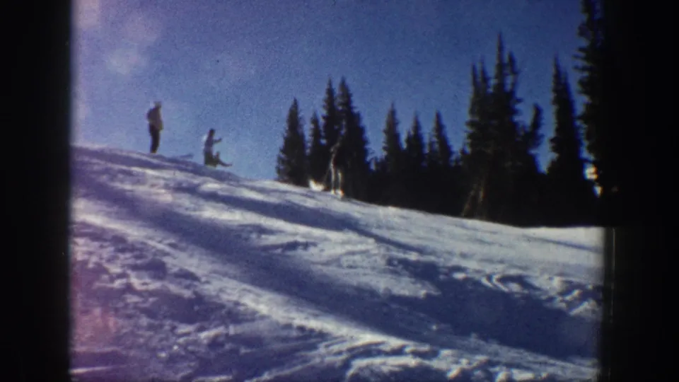 A 1961 Aspen ski-slope frame shows distant people on snow with evergreen trees and soft 8mm color grain.