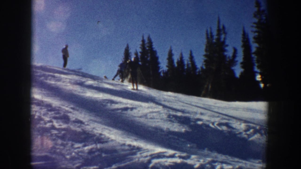 A skier descends a snowy hillside while other figures stand near the ridge.