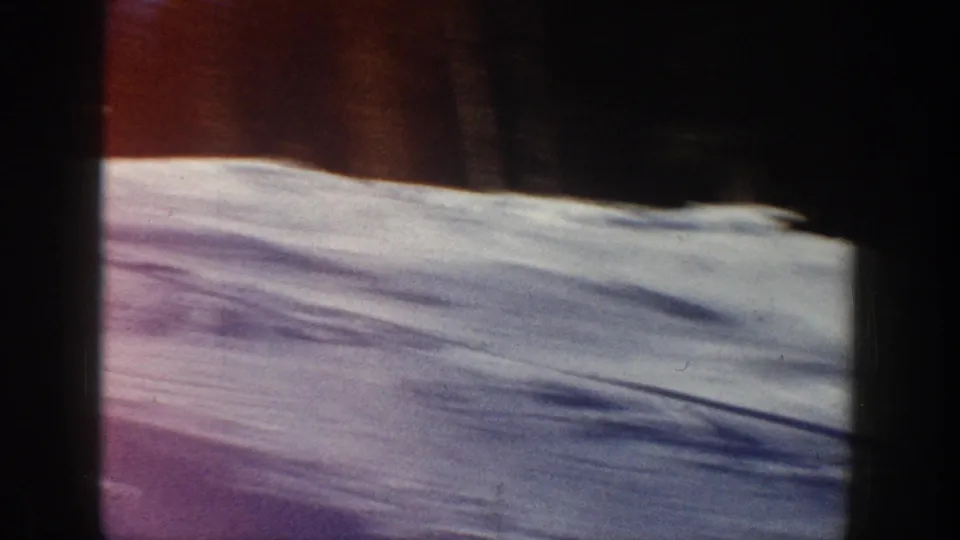 Aspen, Colorado 1961 frame showing a quiet snow-covered slope with ski tracks, shadows, and a dark tree line at the top edge.