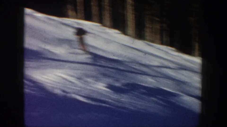 A distant skier moves down a snow-covered slope in Aspen, Colorado, in 1961, framed by evergreen trees and 8mm film borders.