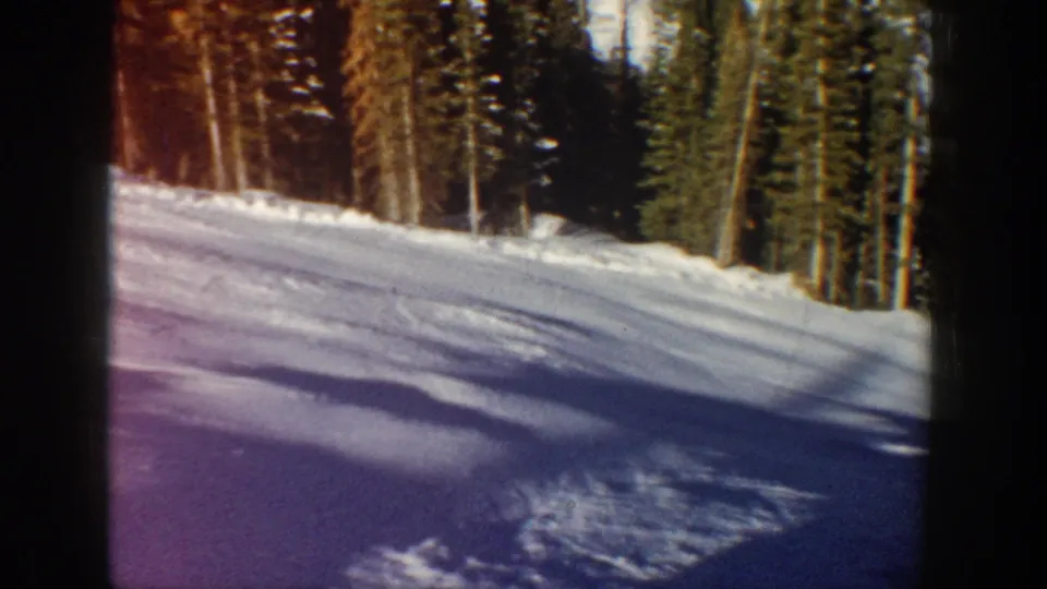 The 1961 Aspen ski scene shows a sunlit snow slope, evergreen forest edge, film grain, and dark 8mm frame borders.