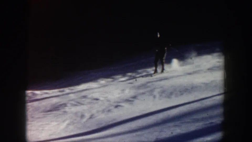 A silhouetted skier crosses a shadowed Aspen slope, with snow spray, long shadows, and visible 8mm grain shaping the frame.