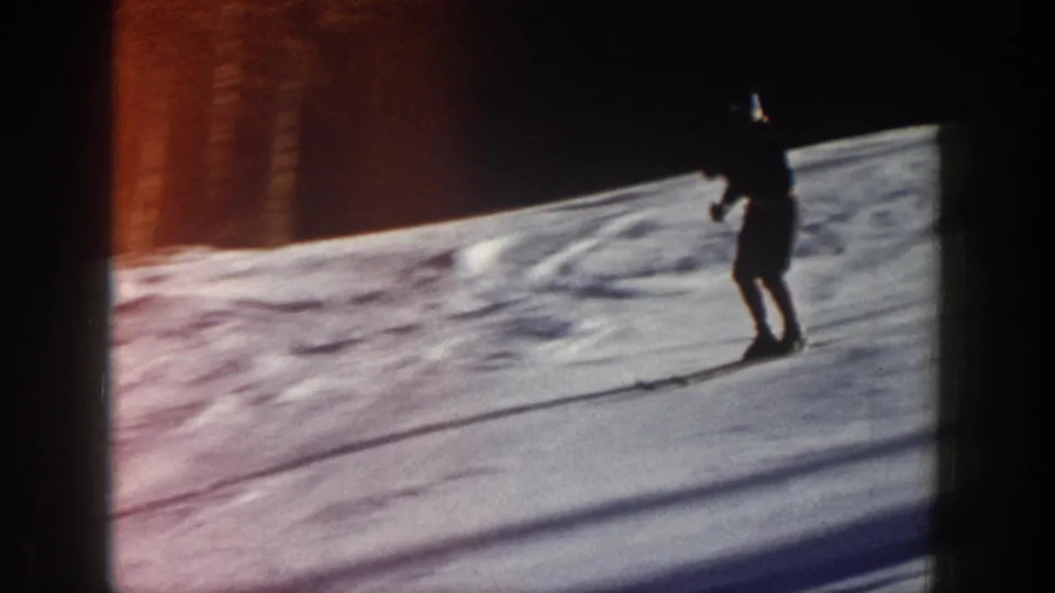 A skier in dark clothing moves across a bright Aspen snowfield, framed by heavy shadow and warm 8mm color shift near the edge.