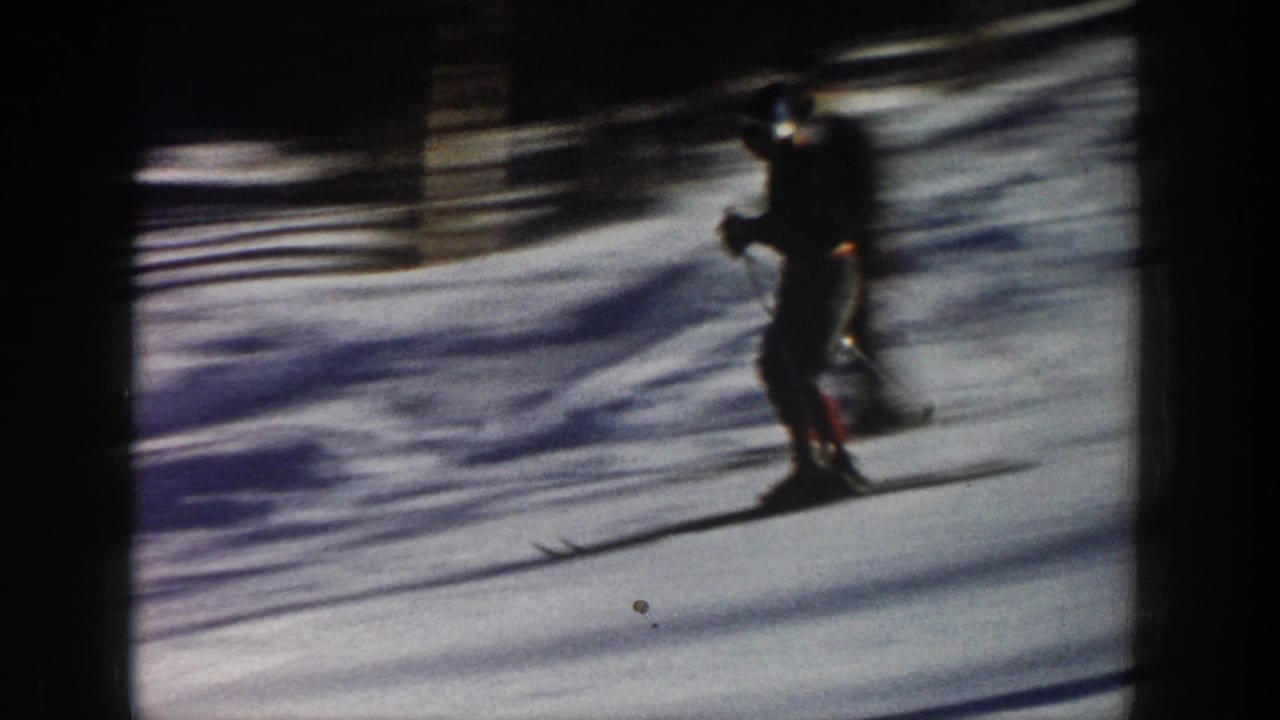 A skier in dark winter clothing glides across snow in Aspen, Colorado, in 1961-era 8mm home-movie footage.