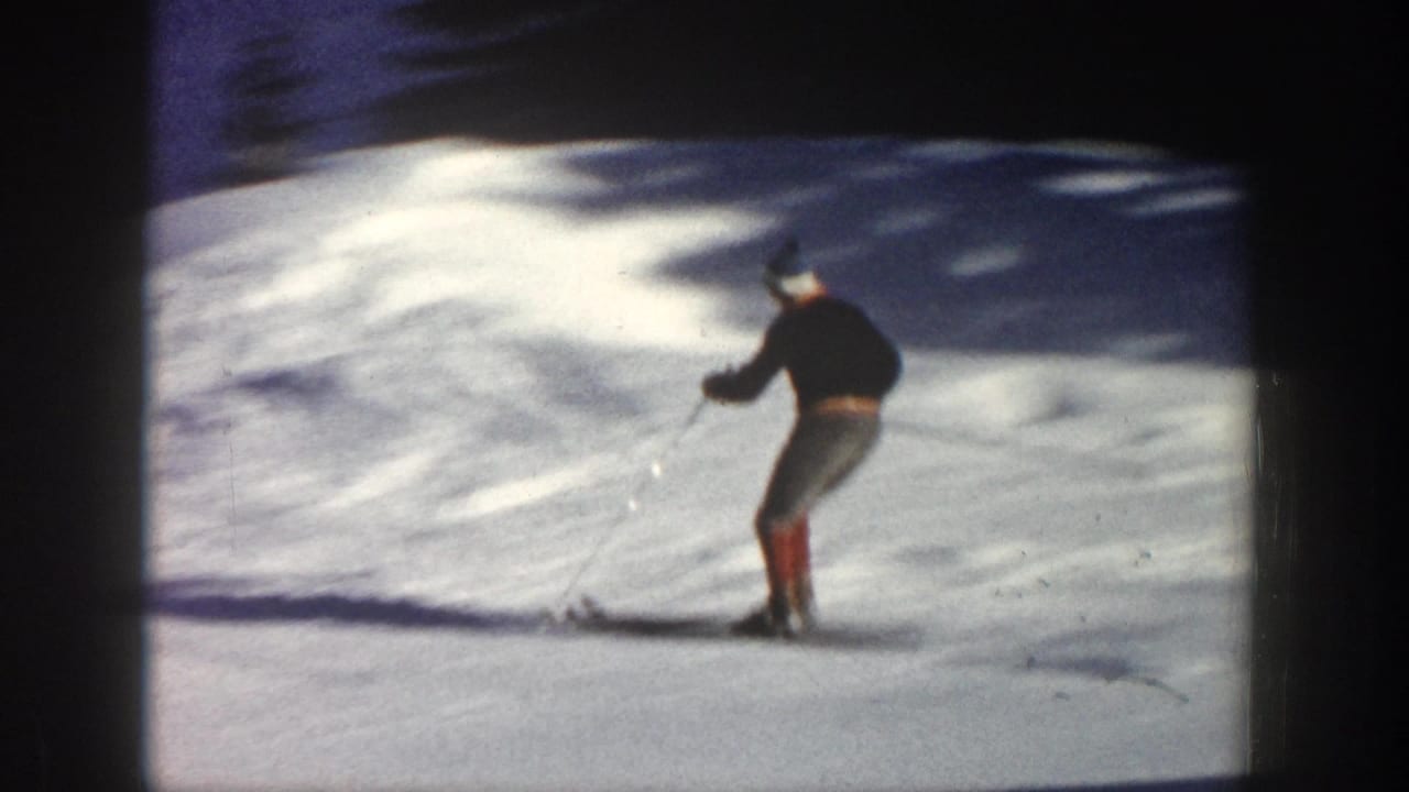 A skier in dark clothing and red boots descends a snowy Aspen slope in grainy 1961 8mm footage.