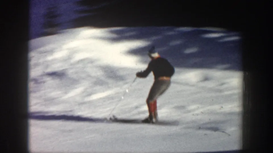 A skier in dark clothing and red boots descends a snowy Aspen slope in grainy 1961 8mm footage.