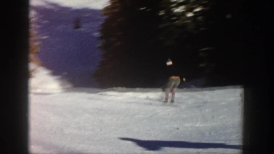 A distant skier travels down a snowy slope beside evergreens in Aspen, Colorado, captured on 8mm home movie film.