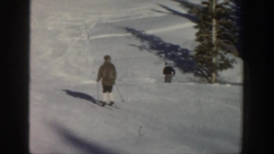 Two skiers appear on a snowy Aspen slope near evergreens in 1961 8mm home-movie footage.