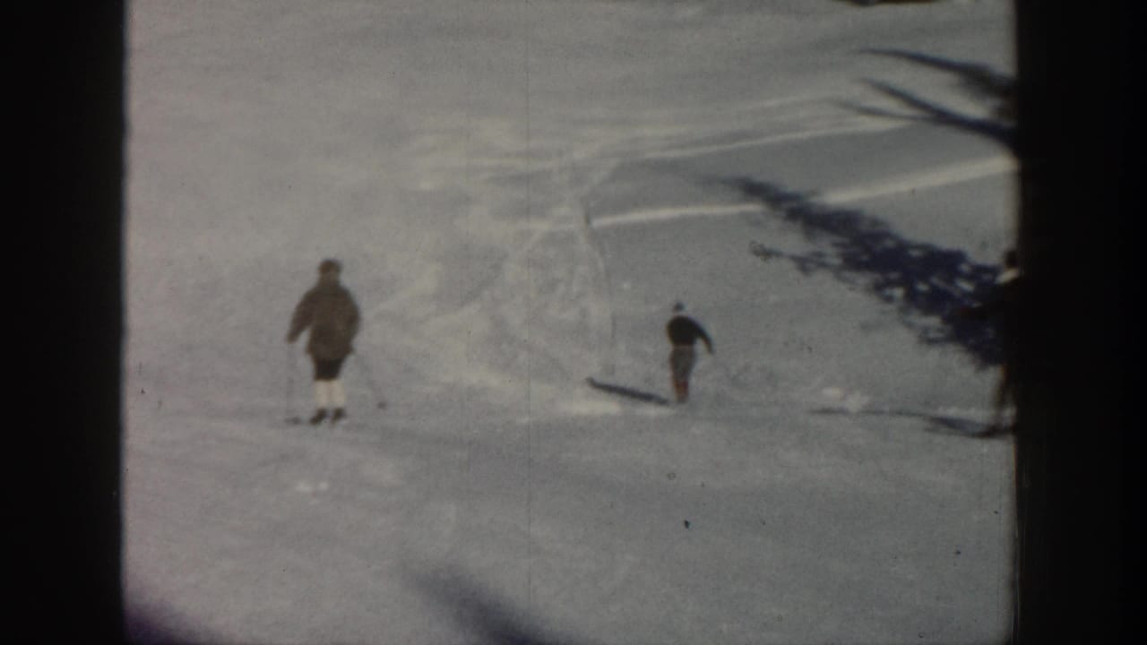 Distant skiers cross a snowy Aspen, Colorado slope in 1961-era 8mm home-movie footage, with evergreen trees at the top of frame.