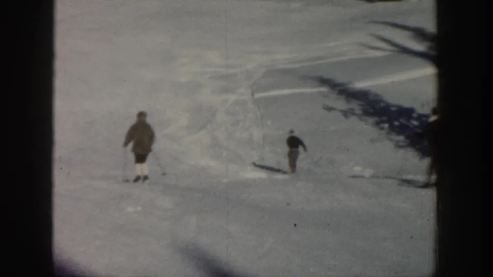 Distant skiers cross a snowy Aspen, Colorado slope in 1961-era 8mm home-movie footage, with evergreen trees at the top of frame.