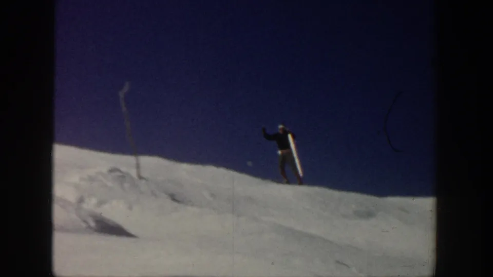A skier with poles stands on a snowy rise in Aspen, Colorado, with blue sky filling much of the 8mm frame.