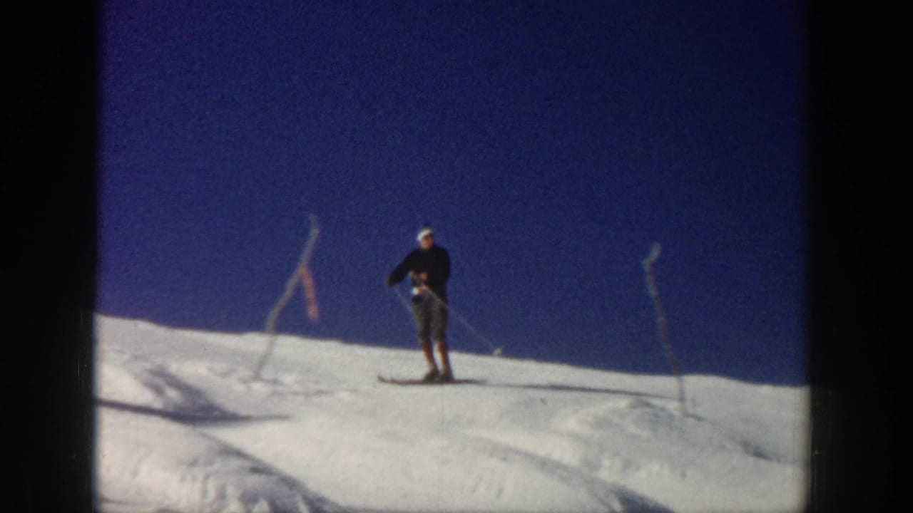 In Aspen, Colorado, a skier in dark clothing and a white hat stands on a bright snowy slope in 1961 8mm footage.