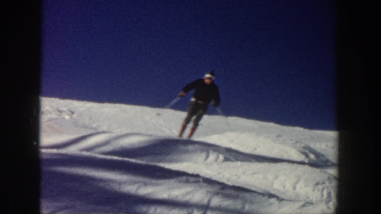 The skier moves across a bumpy Aspen snow slope, holding poles against a clear blue sky in vintage 8mm footage.