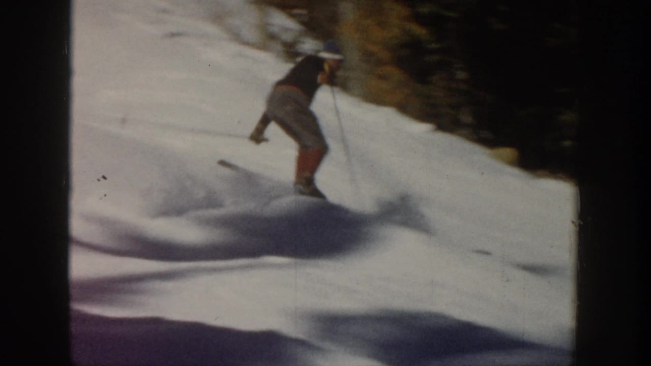 1961 Aspen home-movie frame showing a skier descending a snowy slope beside evergreens, with motion blur and long shadows.