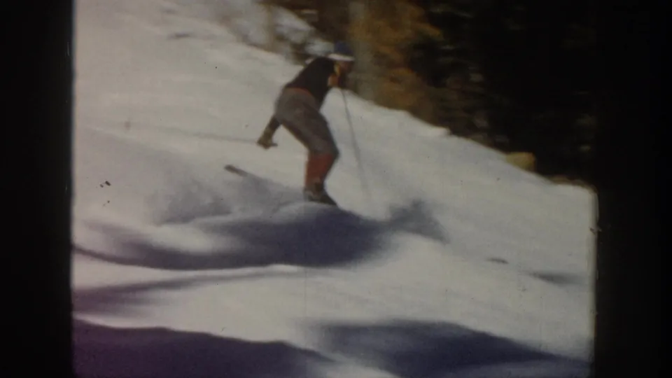 1961 Aspen home-movie frame showing a skier descending a snowy slope beside evergreens, with motion blur and long shadows.