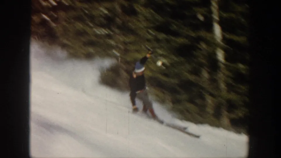 1961 Aspen frame with a skier in winter clothing moving across a bright slope beside dark evergreen trees.