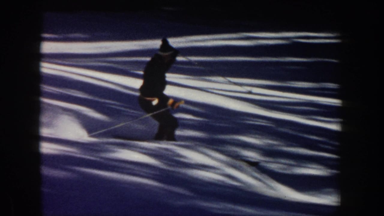 1961 Aspen home-movie frame showing a skier crossing shadowed snow, with strong contrast from trees or terrain outside the frame.