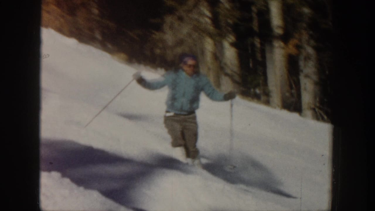 Adult skier in a light blue jacket moving downhill with poles raised.