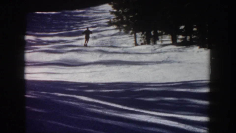 A distant skier descends a snowy Aspen slope in 1961, with evergreen trees and blue shadows framing the run.