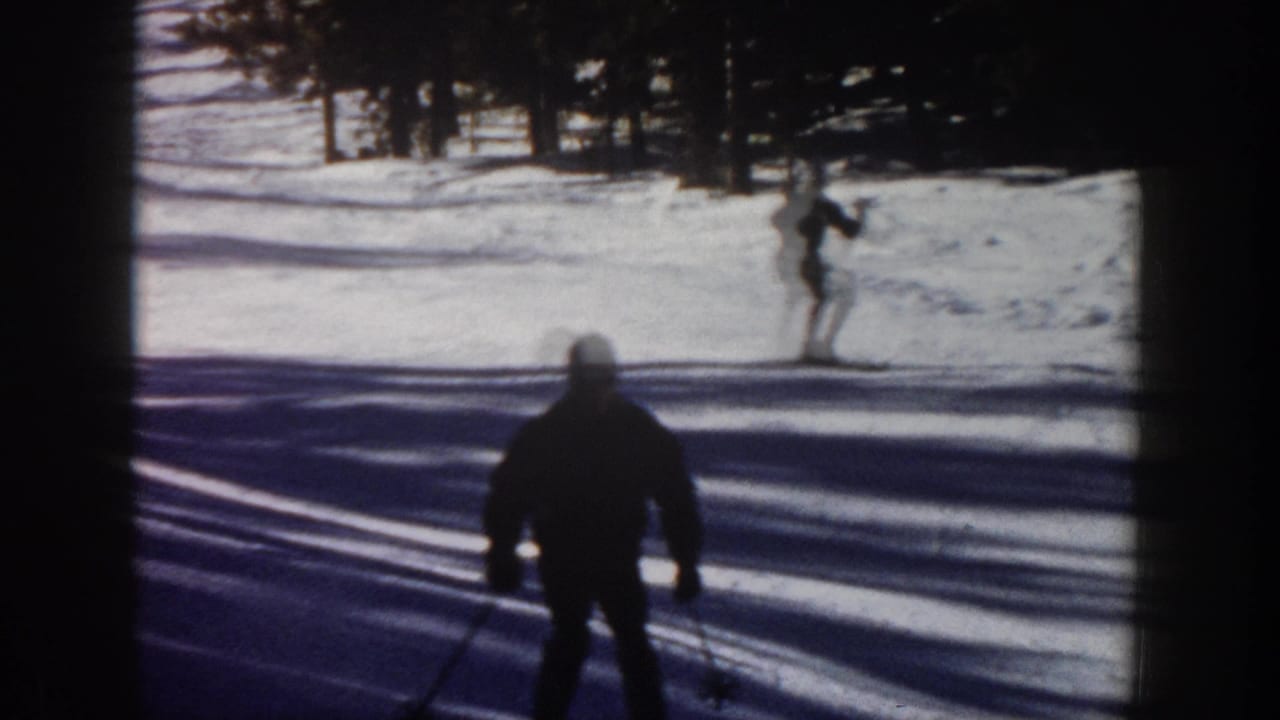 1961 Aspen 8mm frame with a silhouetted skier in the foreground and another skier farther up a snow-covered slope near pine trees.
