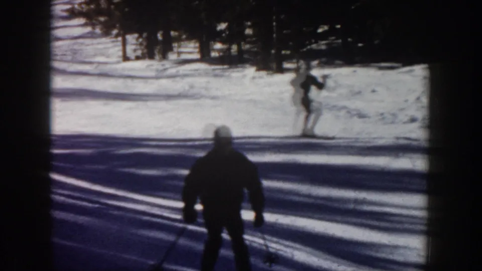 1961 Aspen 8mm frame with a silhouetted skier in the foreground and another skier farther up a snow-covered slope near pine trees.