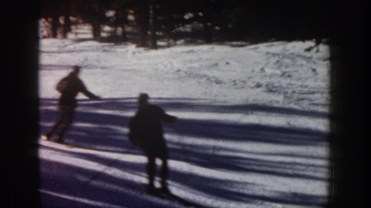 1961 Aspen 8mm frame showing two skiers on a snow-covered downhill area, with pine trees and long shadows behind them.