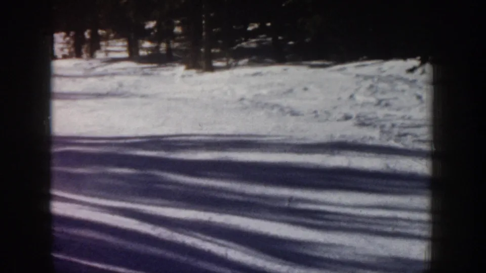 1961 Aspen 8mm frame with an open snow-covered slope, long tree shadows, and a dark pine stand at the top of the frame.