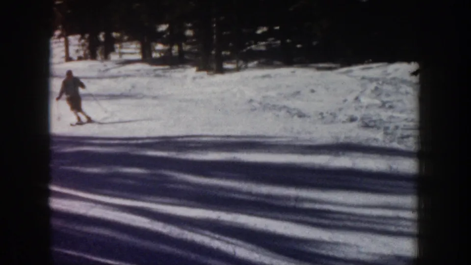 1961 Aspen 8mm frame showing a single skier moving downhill across snow, with pine trees and broad shadows in the background.