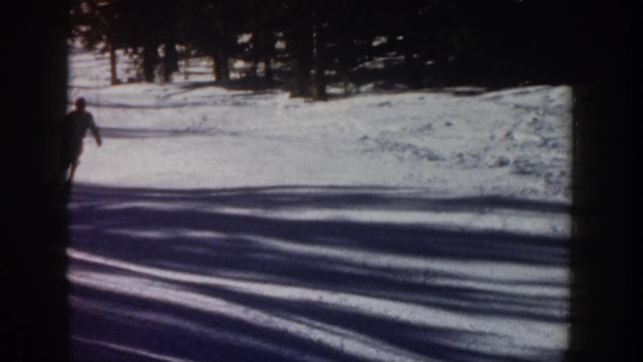 1961 Aspen home-movie frame showing a dark-clothed skier at the left edge of a snowy slope with tree shadows across the snow.