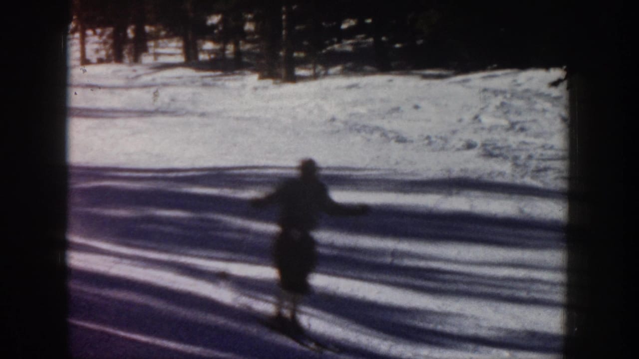 1961 Aspen ski footage frame with a lone skier in dark silhouette crossing bright snow near a line of trees.