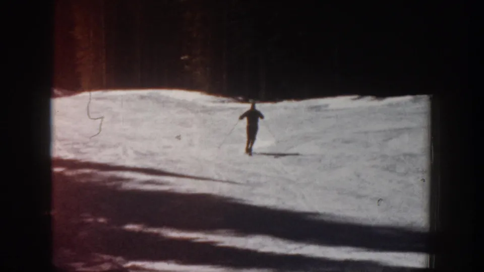 Wide 1961 Aspen home-movie view of a skier on an open snowfield with dark trees and heavy exposure variation.