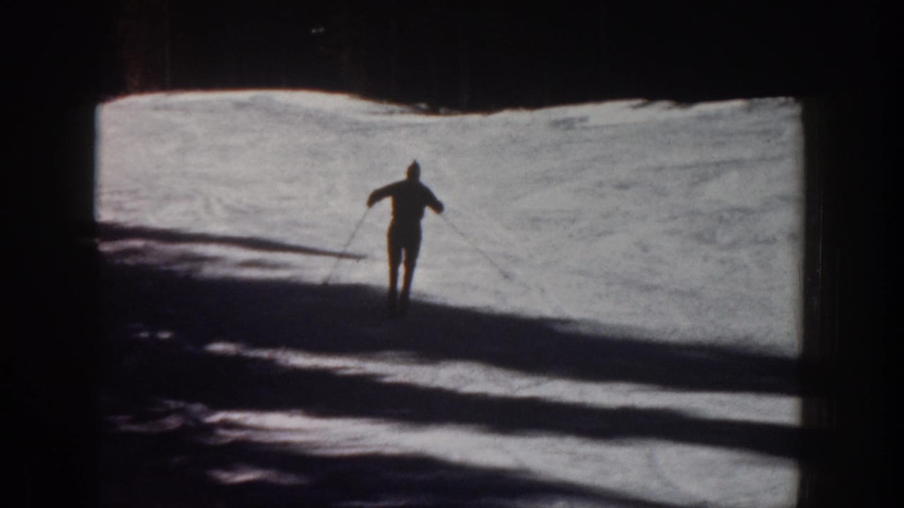1961 Aspen home-movie frame showing a distant lone skier crossing bright snow under strong backlight and long shadows.
