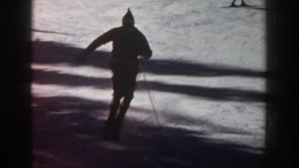 Closer 1961 Aspen home-movie view of the skier passing through deep shadow and bright snow, with poles and winter clothing visible.