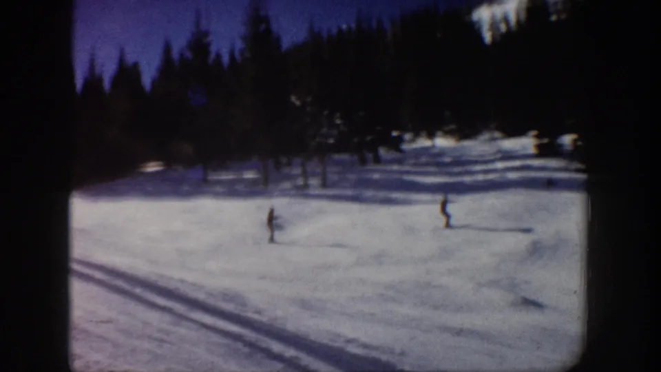 Two skiers appear far apart on a snowy Aspen hillside, framed by evergreens and 8mm film edges.