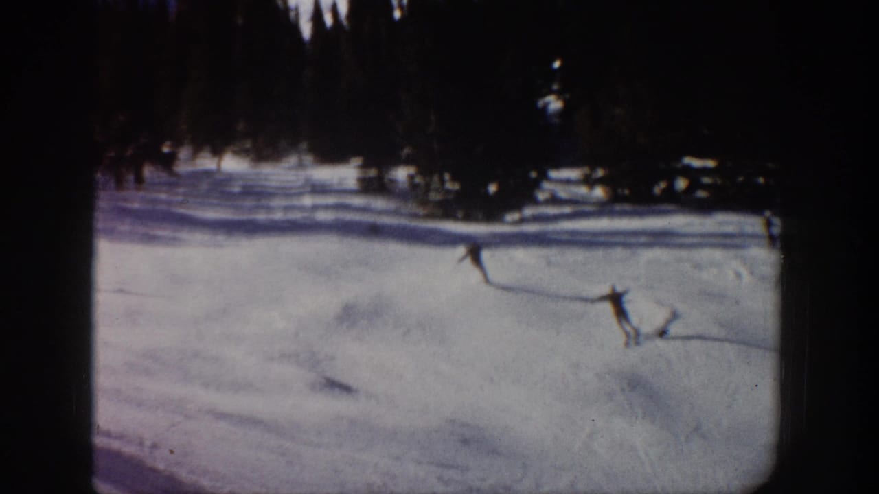 1961 Aspen 8mm frame showing distant skiers on a snow-covered mountain slope with evergreen trees along the top edge.