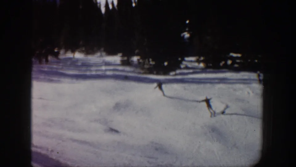 1961 Aspen 8mm frame showing distant skiers on a snow-covered mountain slope with evergreen trees along the top edge.