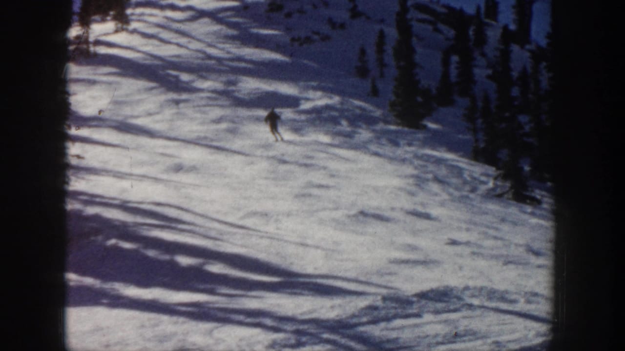 Distant skier on an Aspen, Colorado snowy slope in 1961 home-movie footage, framed by evergreens and long shadows.