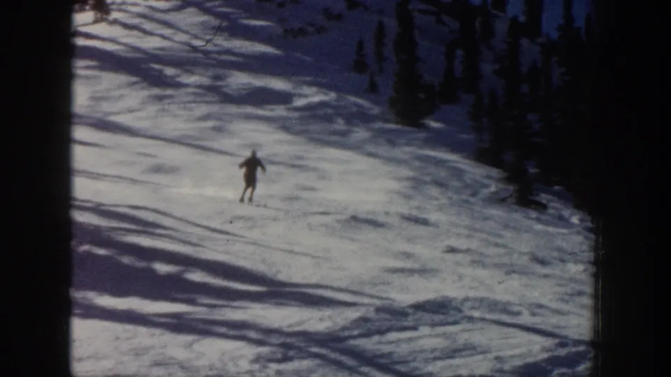 A distant skier reaches the lower part of the Aspen snow slope, surrounded by evergreens and dark film-frame edges.