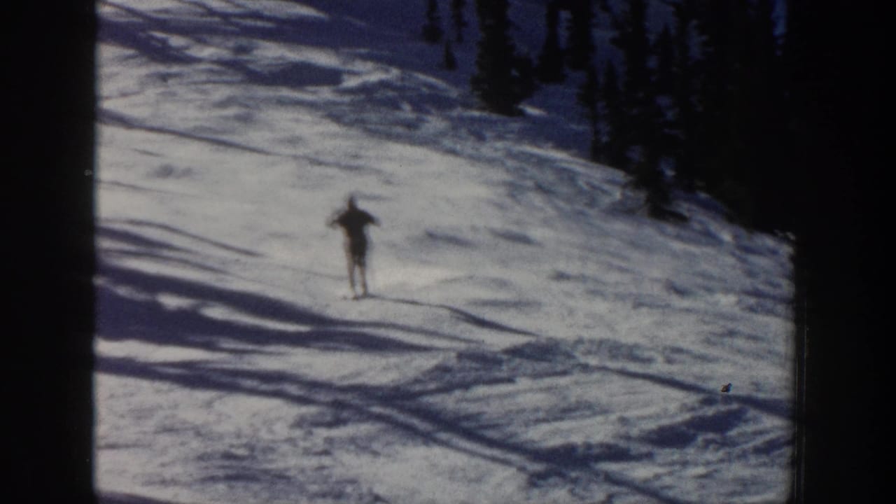 A skier in dark winter gear descends a snowy Aspen hillside, softened by motion blur and 8mm film grain.