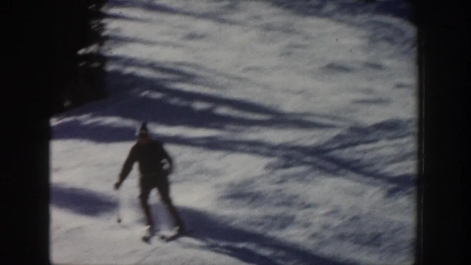 A closer view of the skier in dark winter clothing gliding down the Aspen snowfield, with motion blur and strong shadow bands.