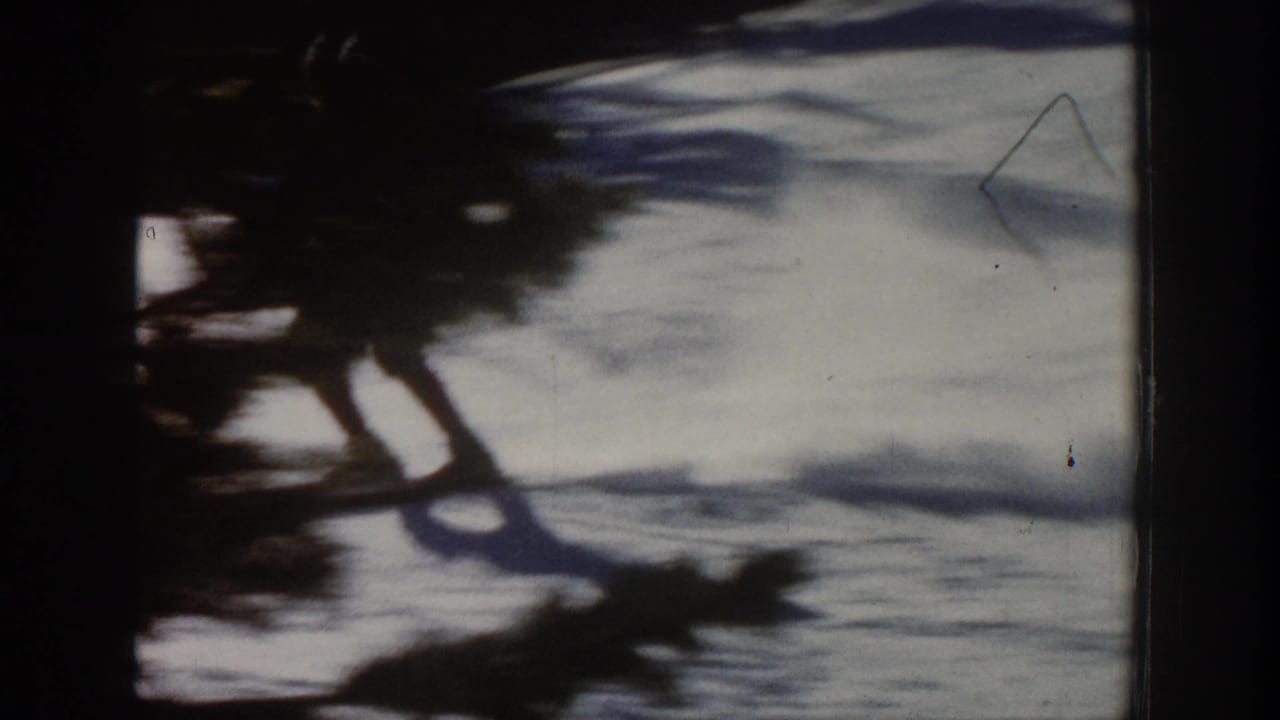1961 Aspen 8mm frame showing a skier in dark winter clothing crossing bright snow with a long shadow nearby.